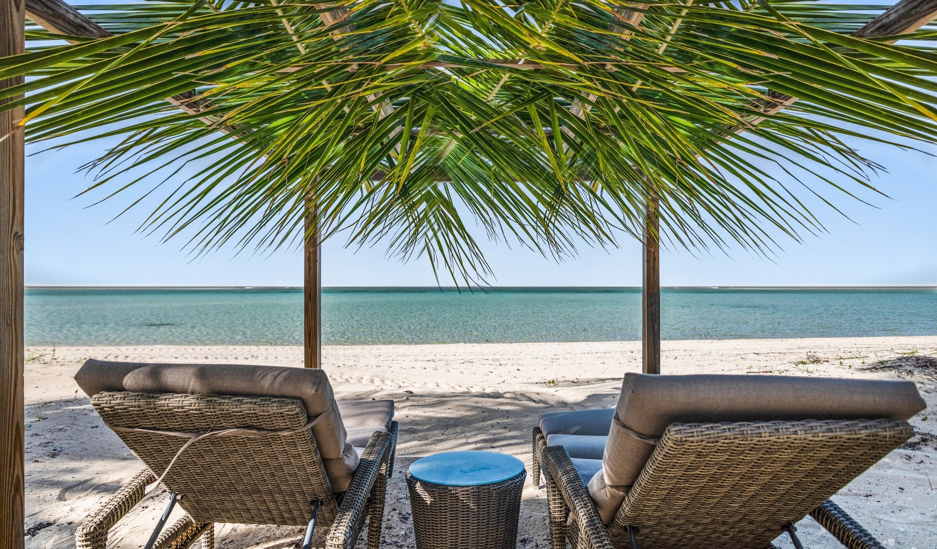 2 deck chairs under palm leaves at honeymoon spot Kamalame Cay