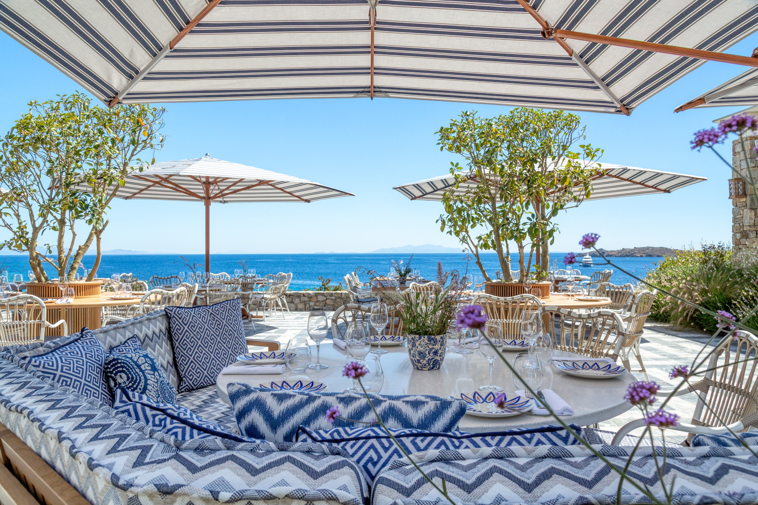 Outdoor seating area with striped umbrellas, tables, and chairs by a body of water. Elias restaurant Santa Marina