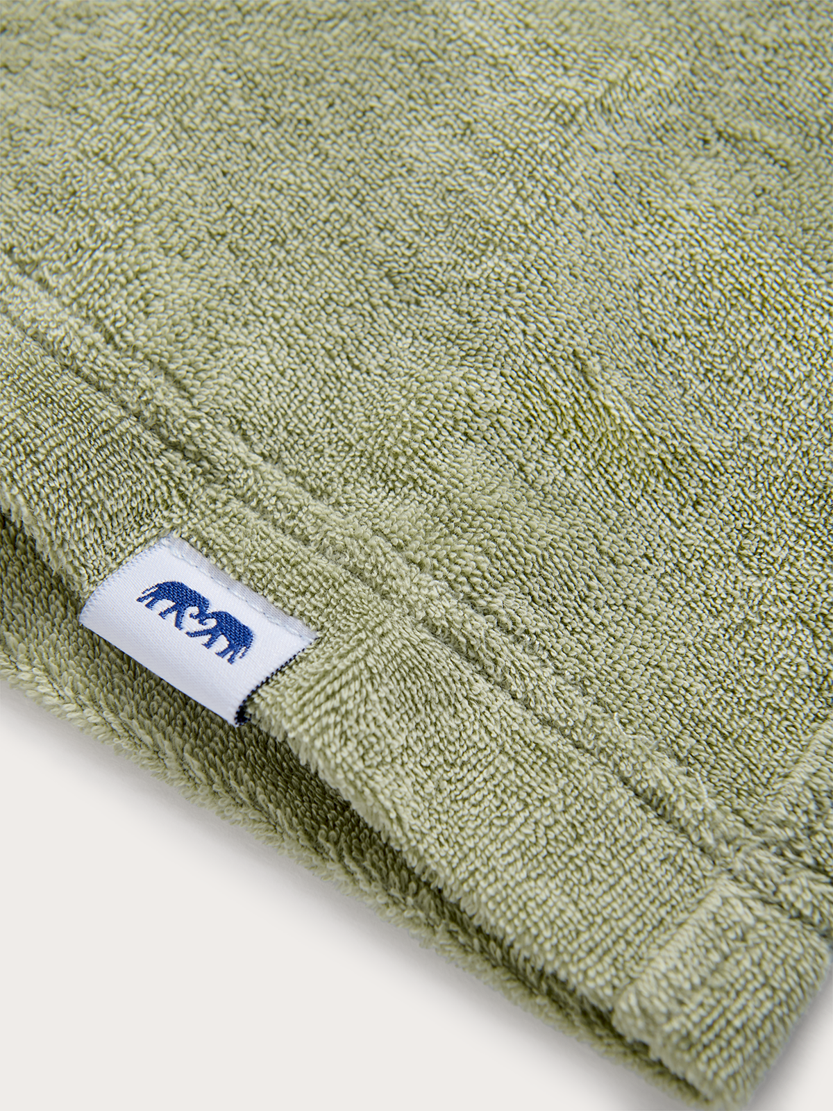 Close-up of green towel shorts for kids with a brand label featuring two elephants on a white background