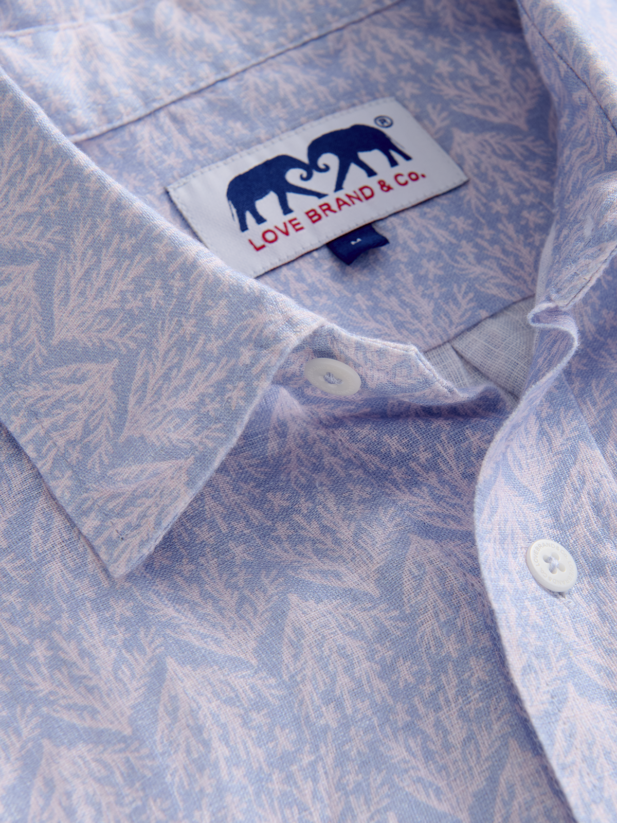 Close-up of a light blue and purple patterned shirt with a brand label featuring two elephants and the text 'LOVE BRAND & CO.'