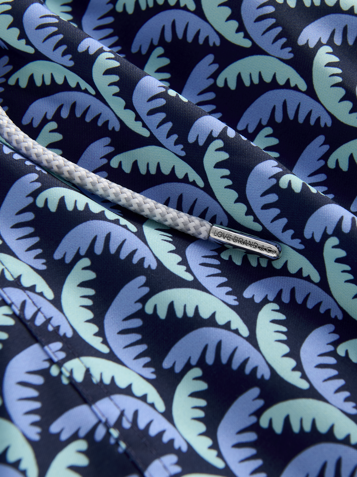Close-up of a patterned fabric with blue and green leaf design on a dark background.