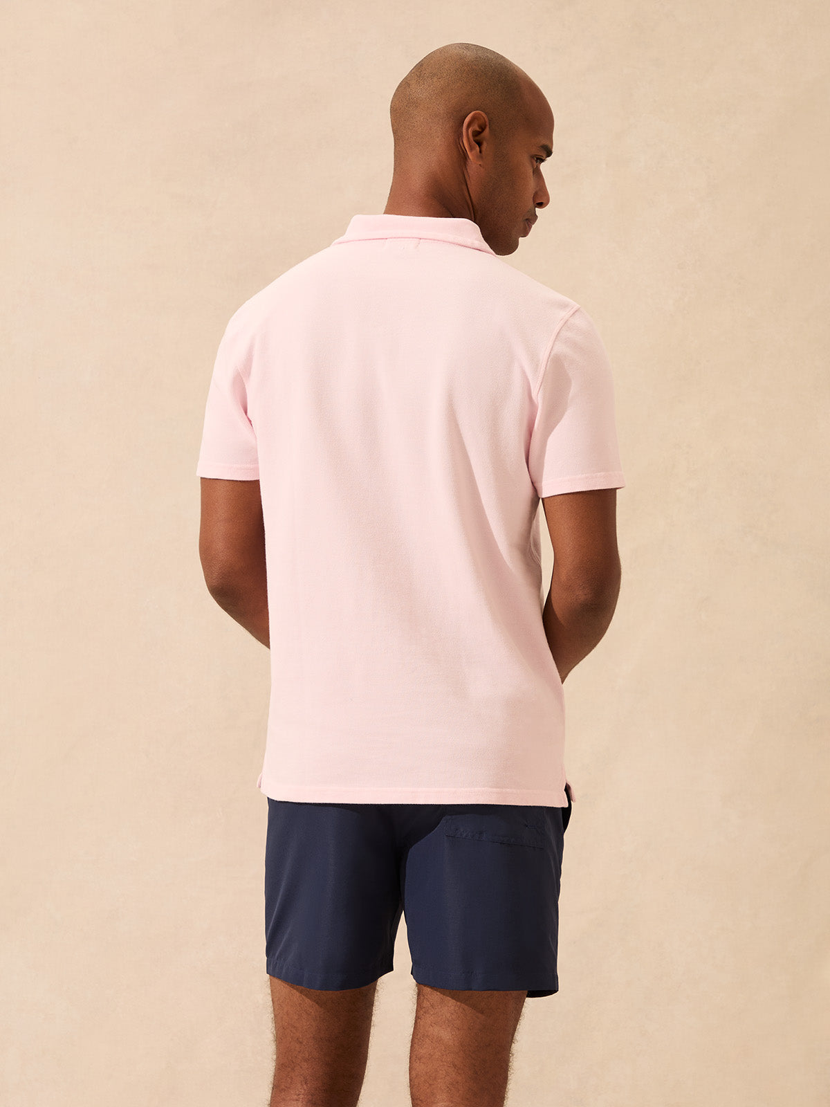 Man wearing a light pink polo shirt and navy shorts on a beige background