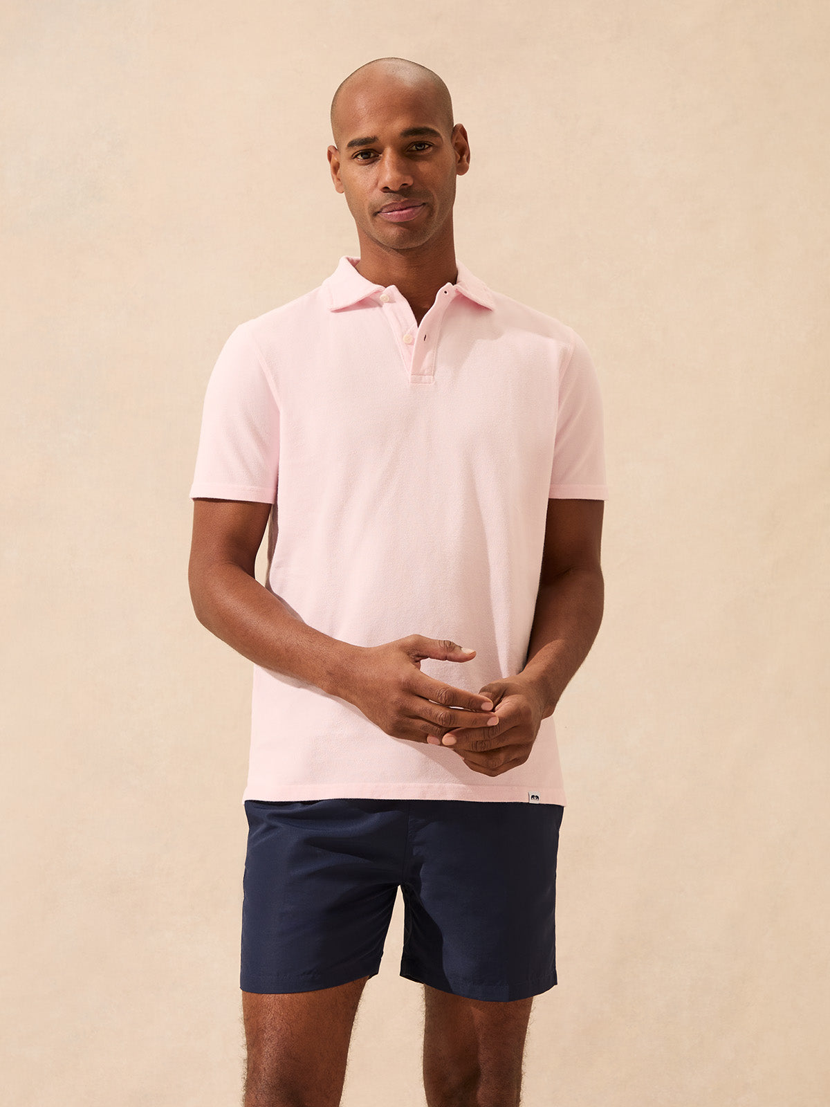 Man wearing a light pink polo shirt and navy shorts against a beige background