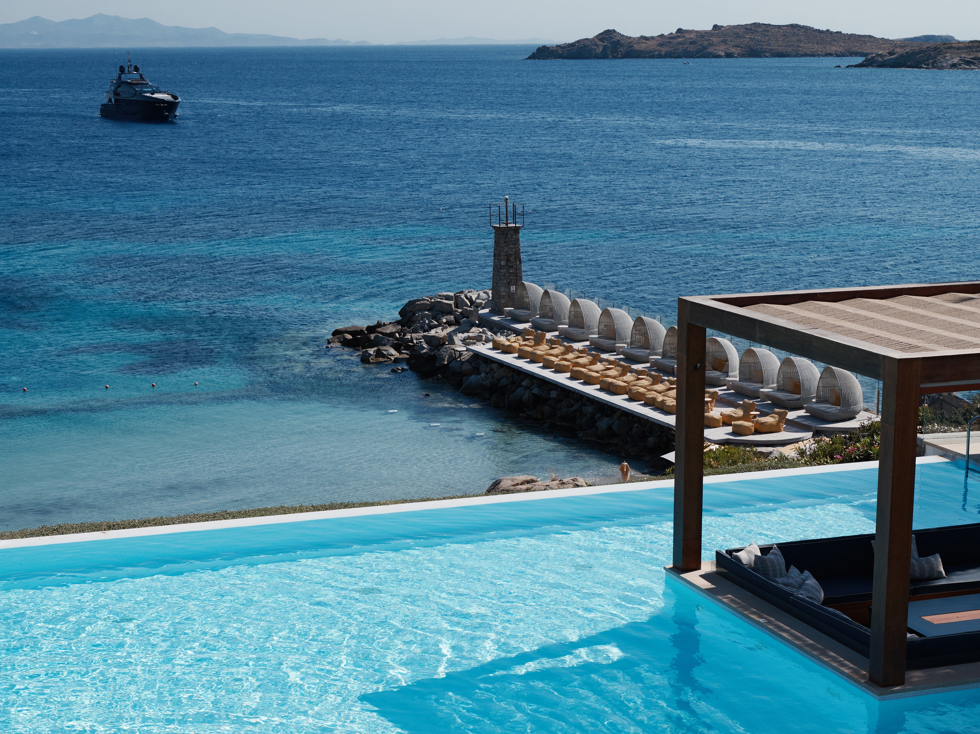 Infinity pool with ocean view, lounge chairs, and a boat in the distance.