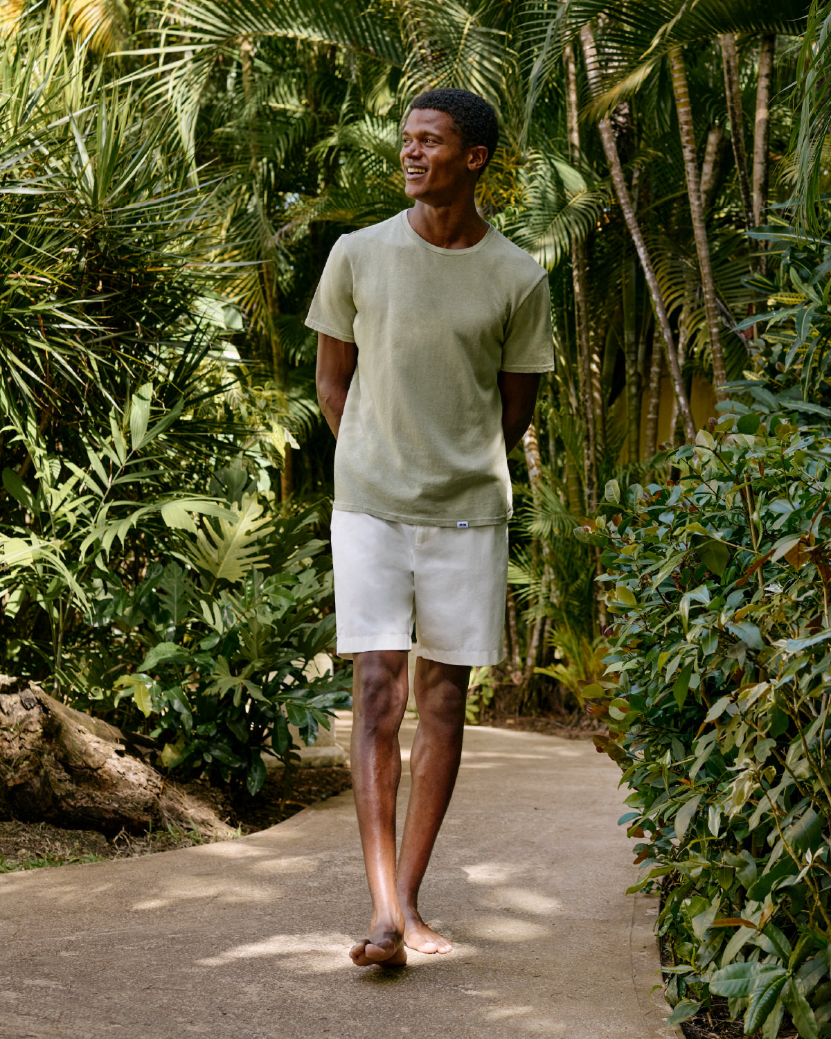 Man walking on a path wearing a green t-shirt and white shorts surrounded by tropical plants