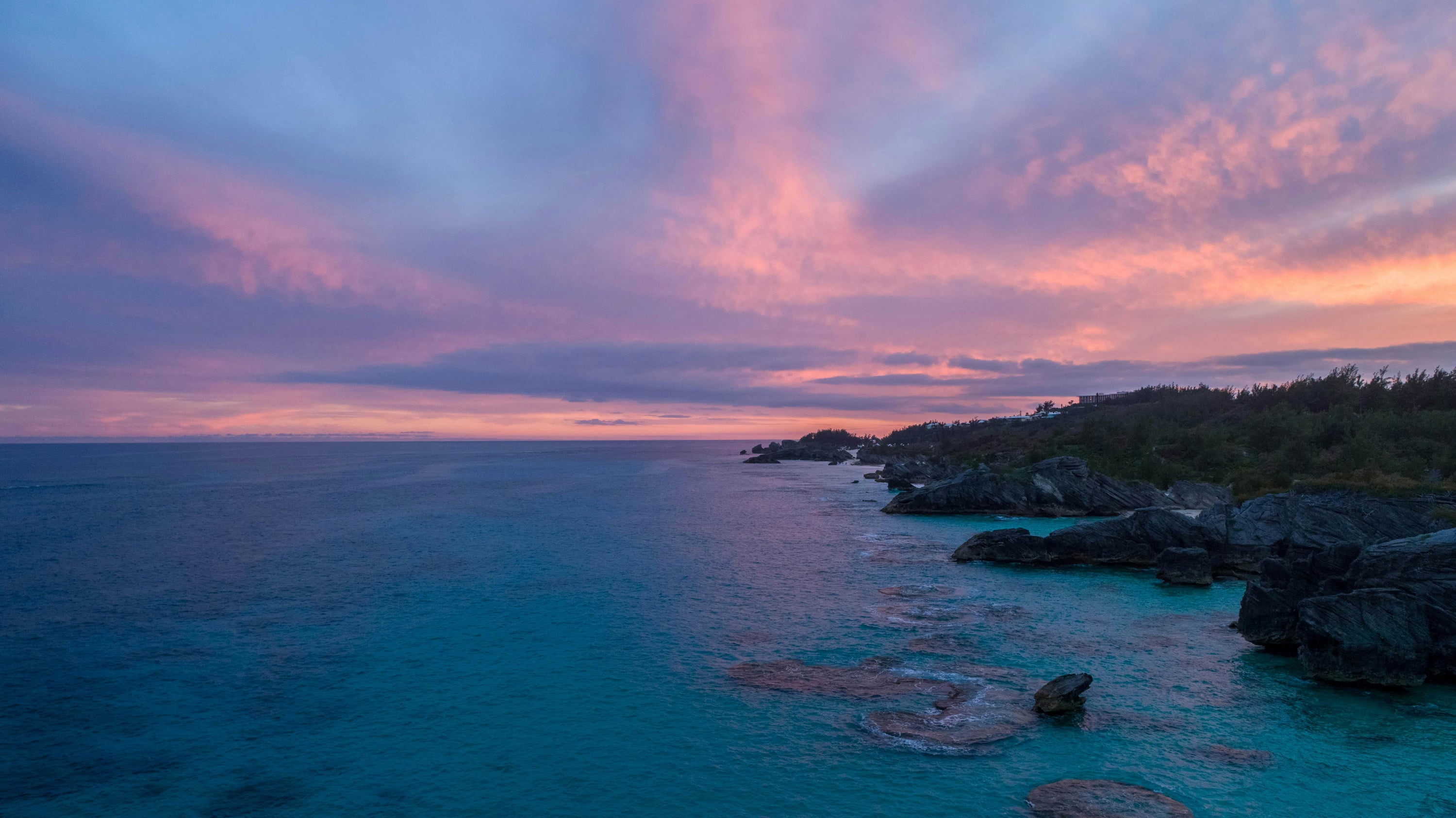 Sunset over a rocky Bermuda coastline with vibrant blue and pink hues.