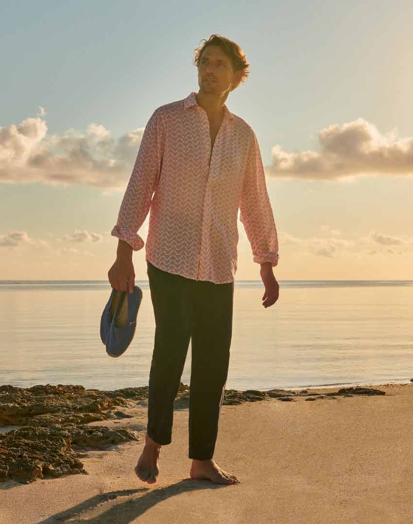 model on the beach wears love brand pink linen shirt, chinos and carries espadrilles