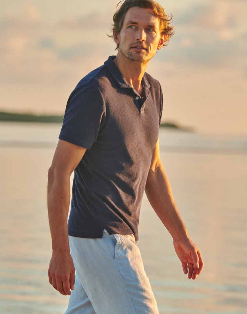 model wears love brand terry towelling navy blue polo shirt styled with linen trousers