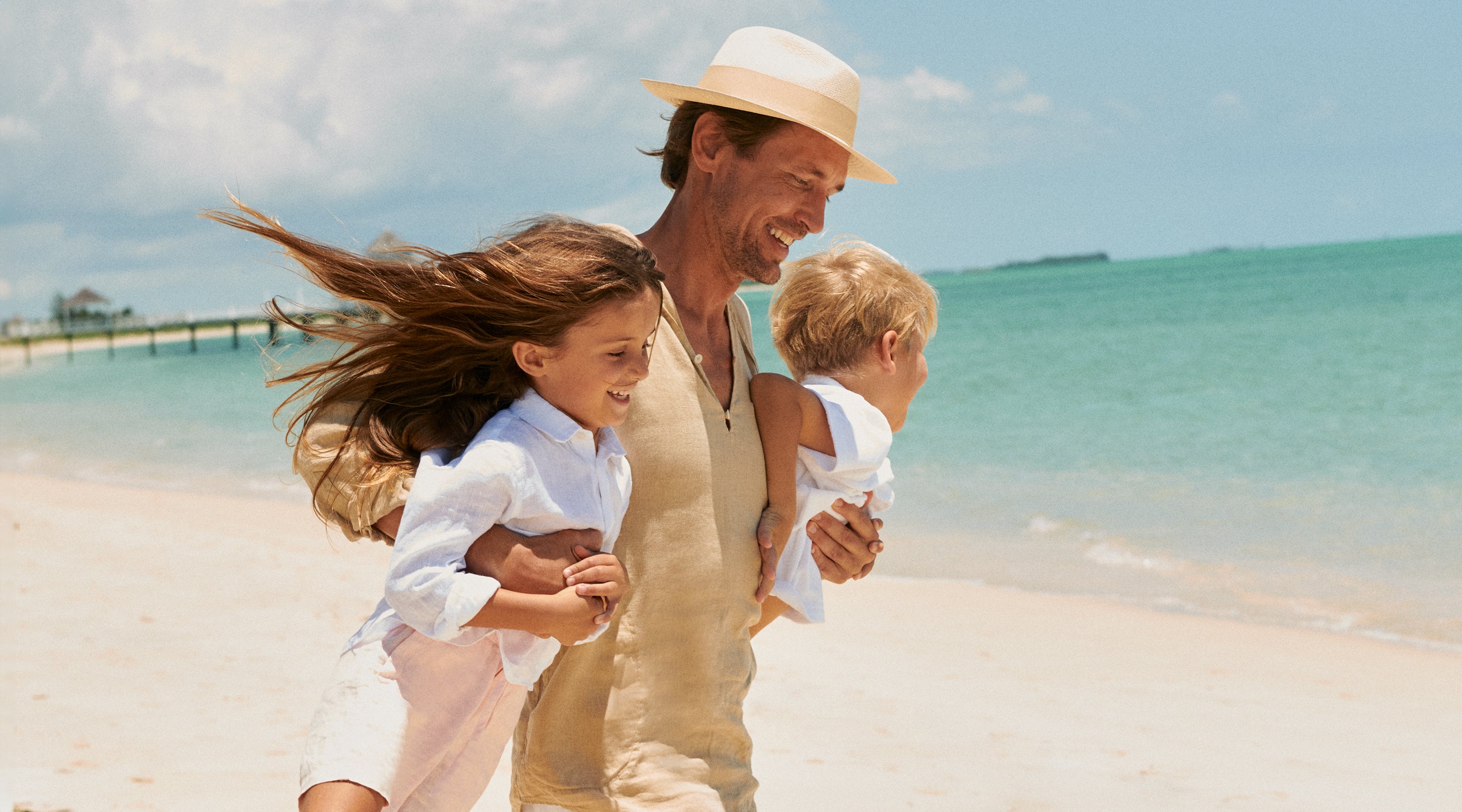 father carries his two children on a beach