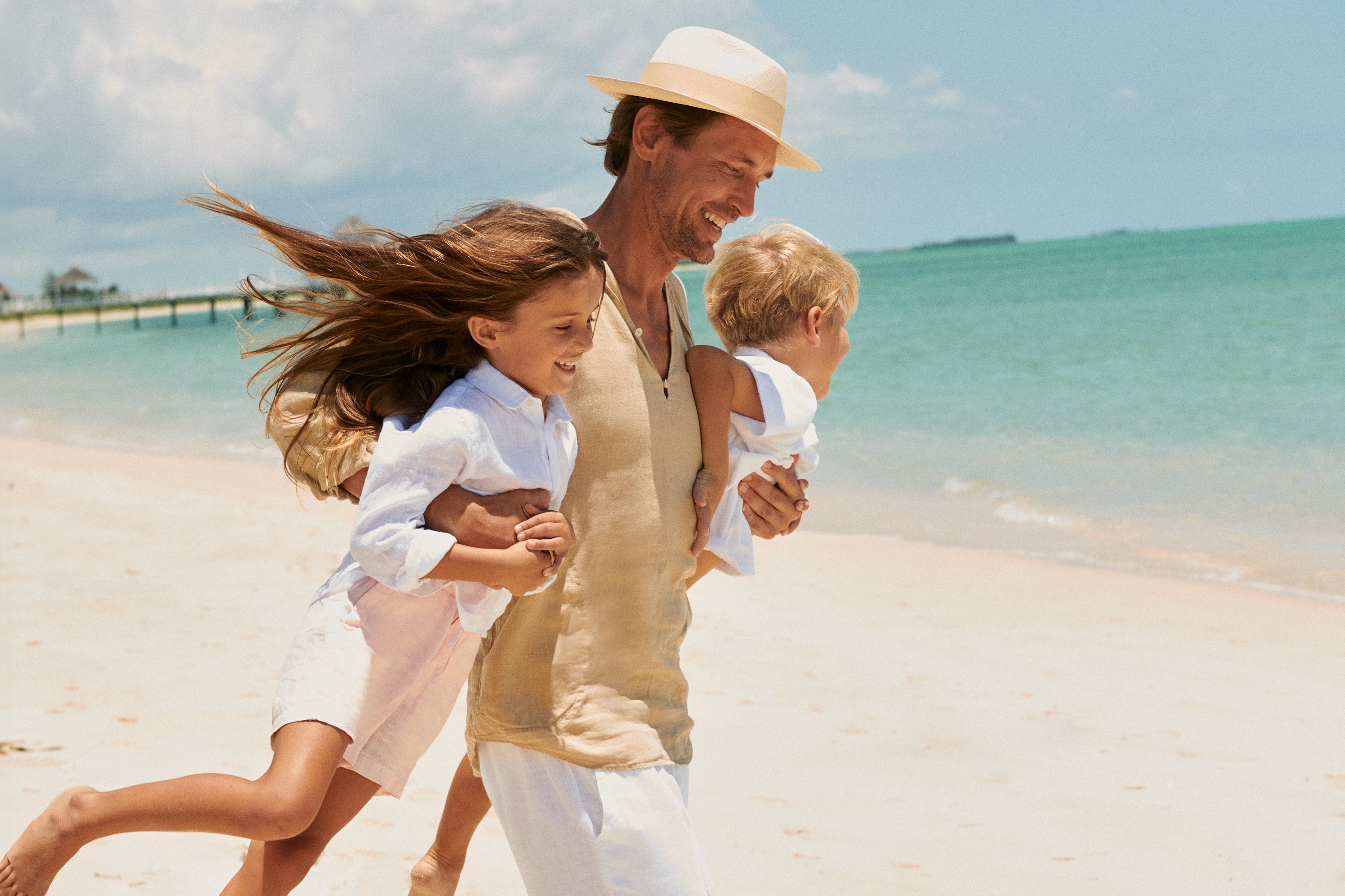 Man with two children running on a beach wearing linen shirts.