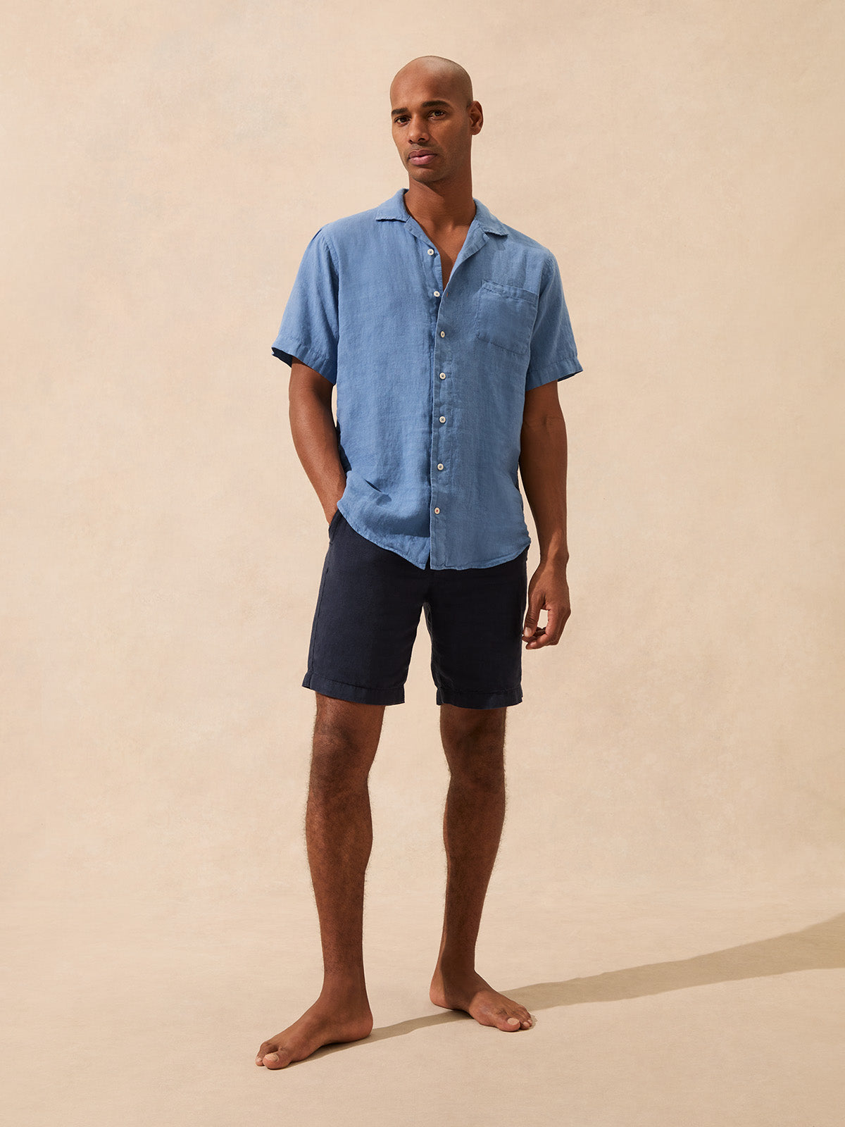 Man wearing a short sleeve blue linen shirt and shorts on a beige background
