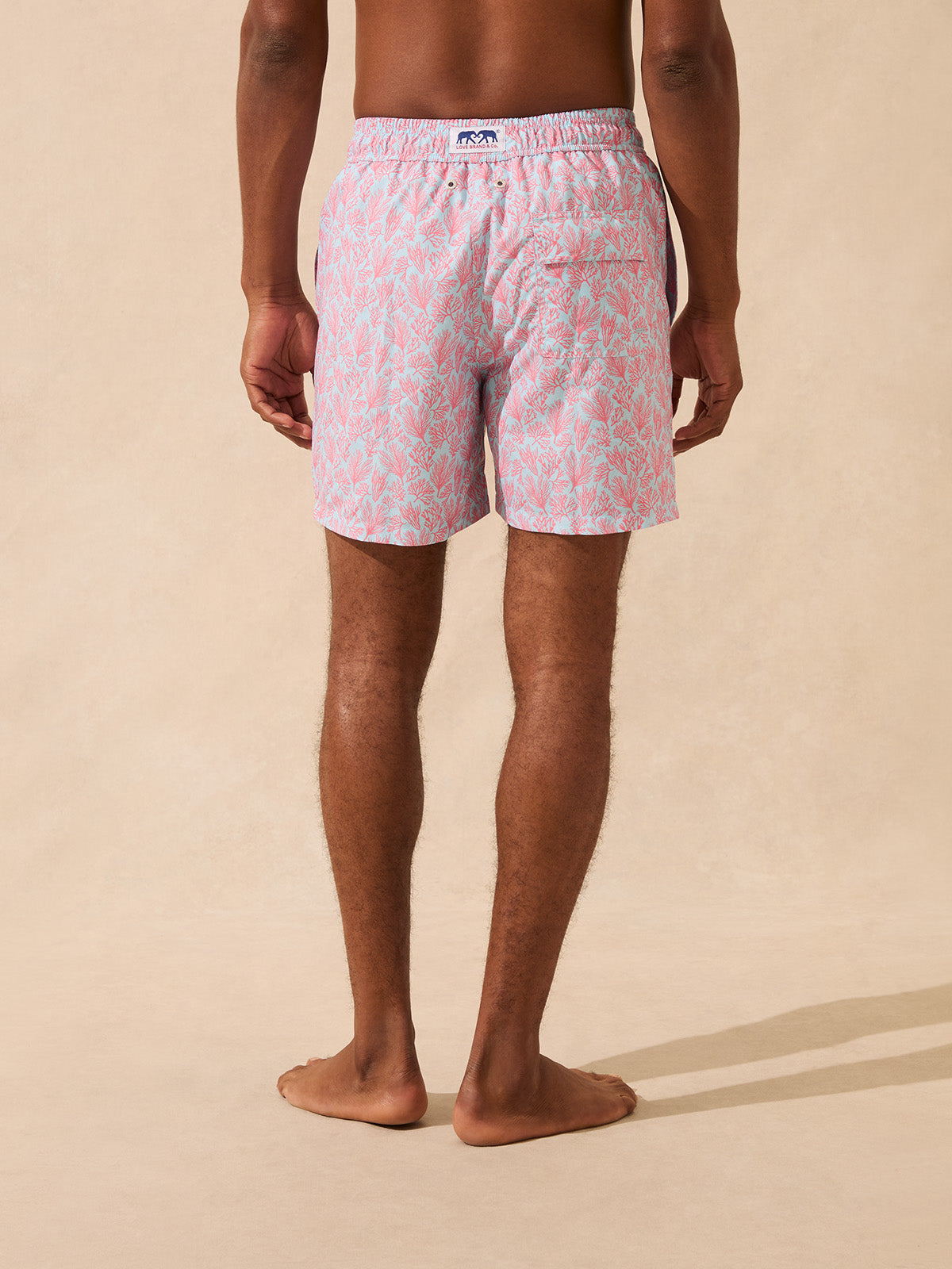 Back view of a man wearing light blue swim shorts with a pink coral pattern
