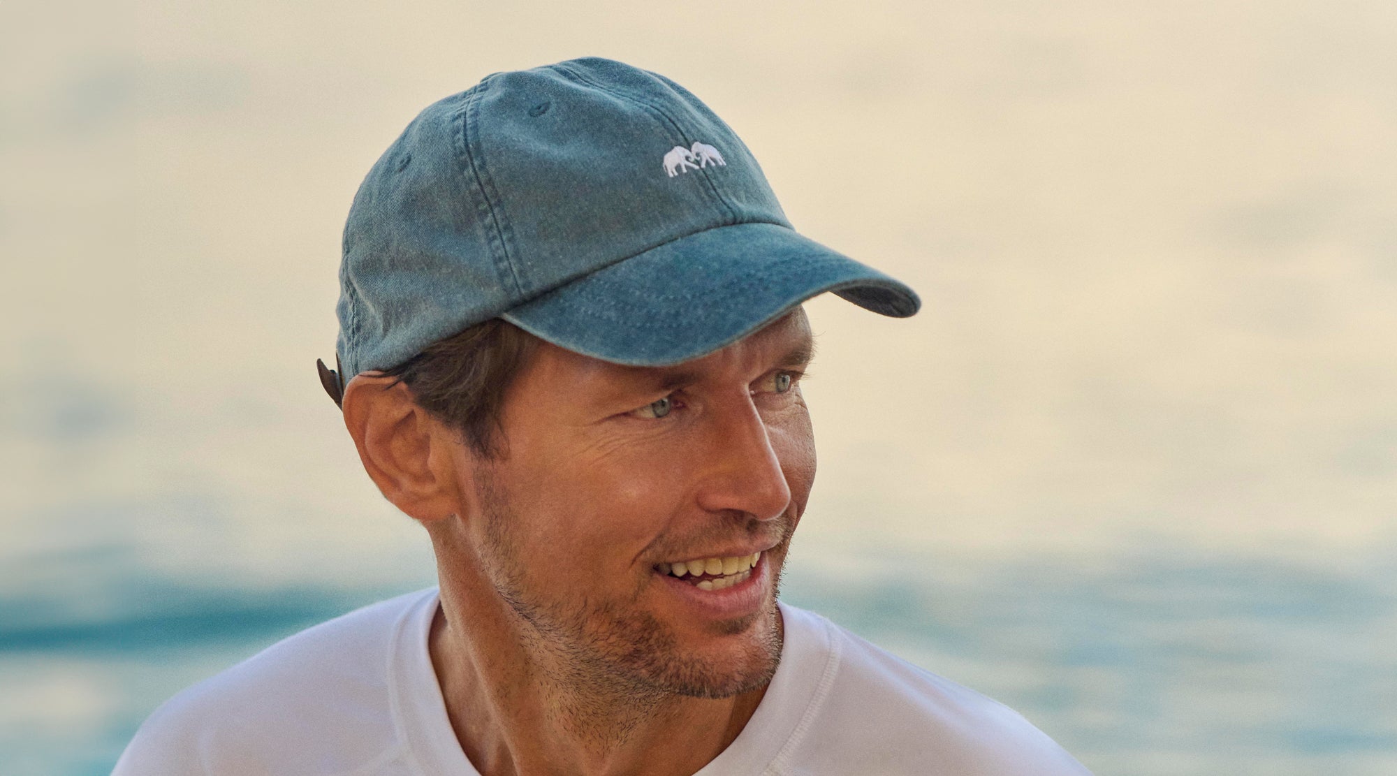 Man wearing a blue baseball cap with a logo, standing against a blurred natural background