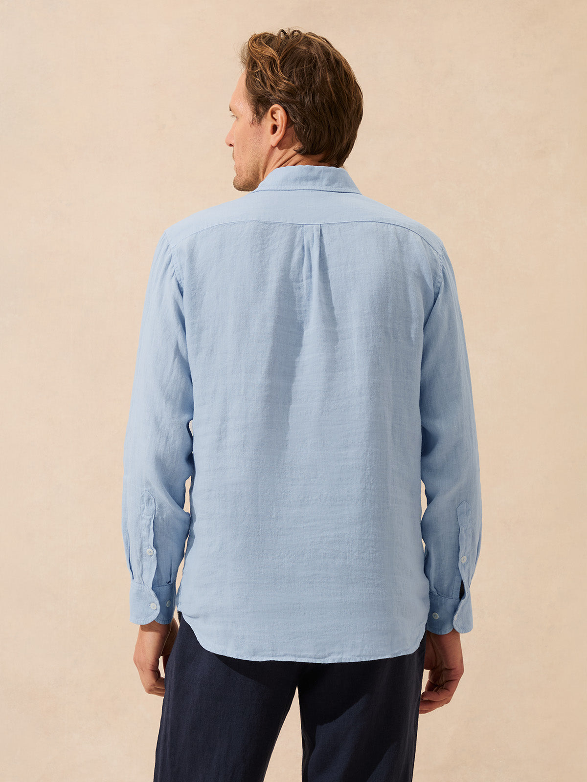 Back view of man wearing a light blue shirt against a beige background