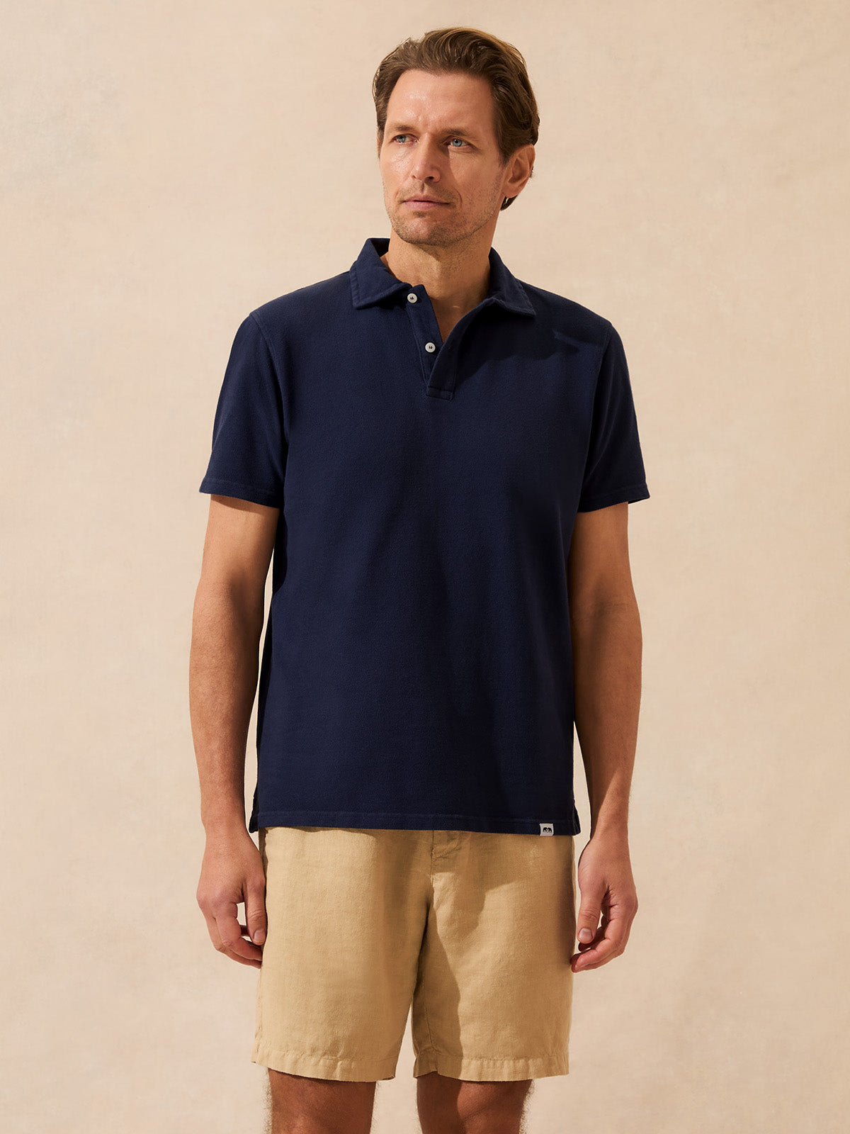 Man wearing a navy polo shirt and beige shorts against a beige background