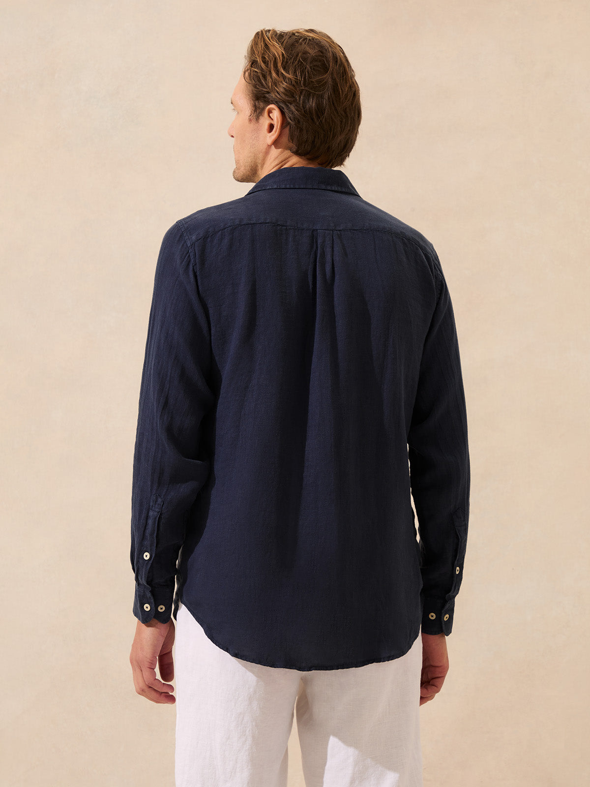 Man wearing a navy blue linen shirt and white pants against a beige background