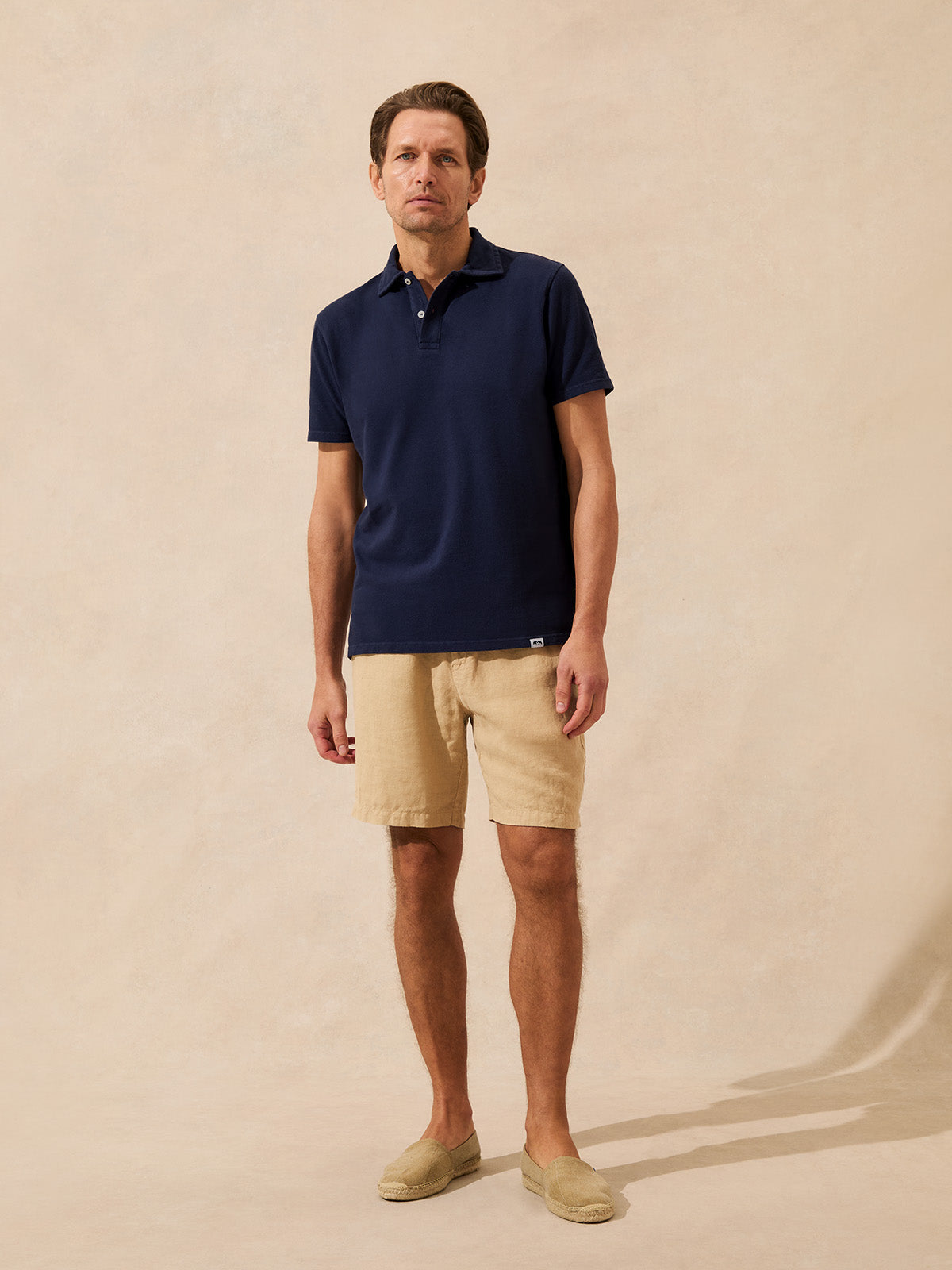 Man wearing a navy polo shirt and beige shorts against a beige background