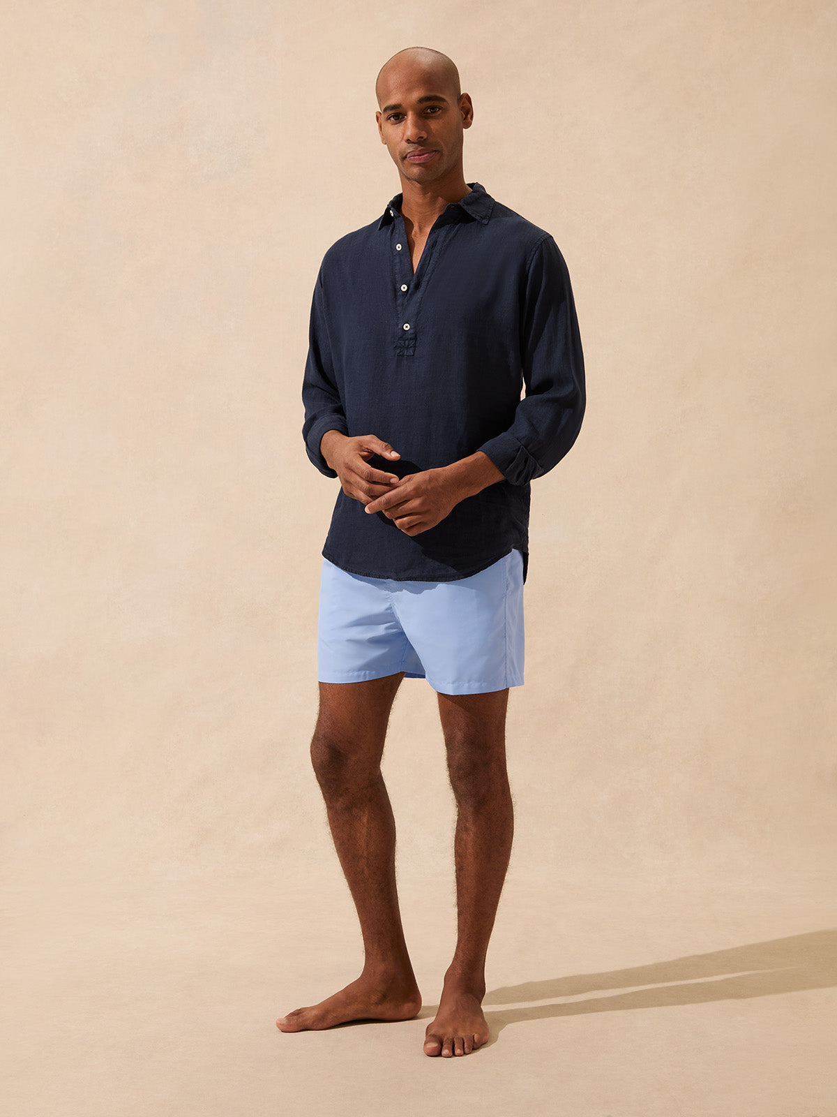 Man wearing a navy long-sleeve shirt and light blue swim shorts against a beige background