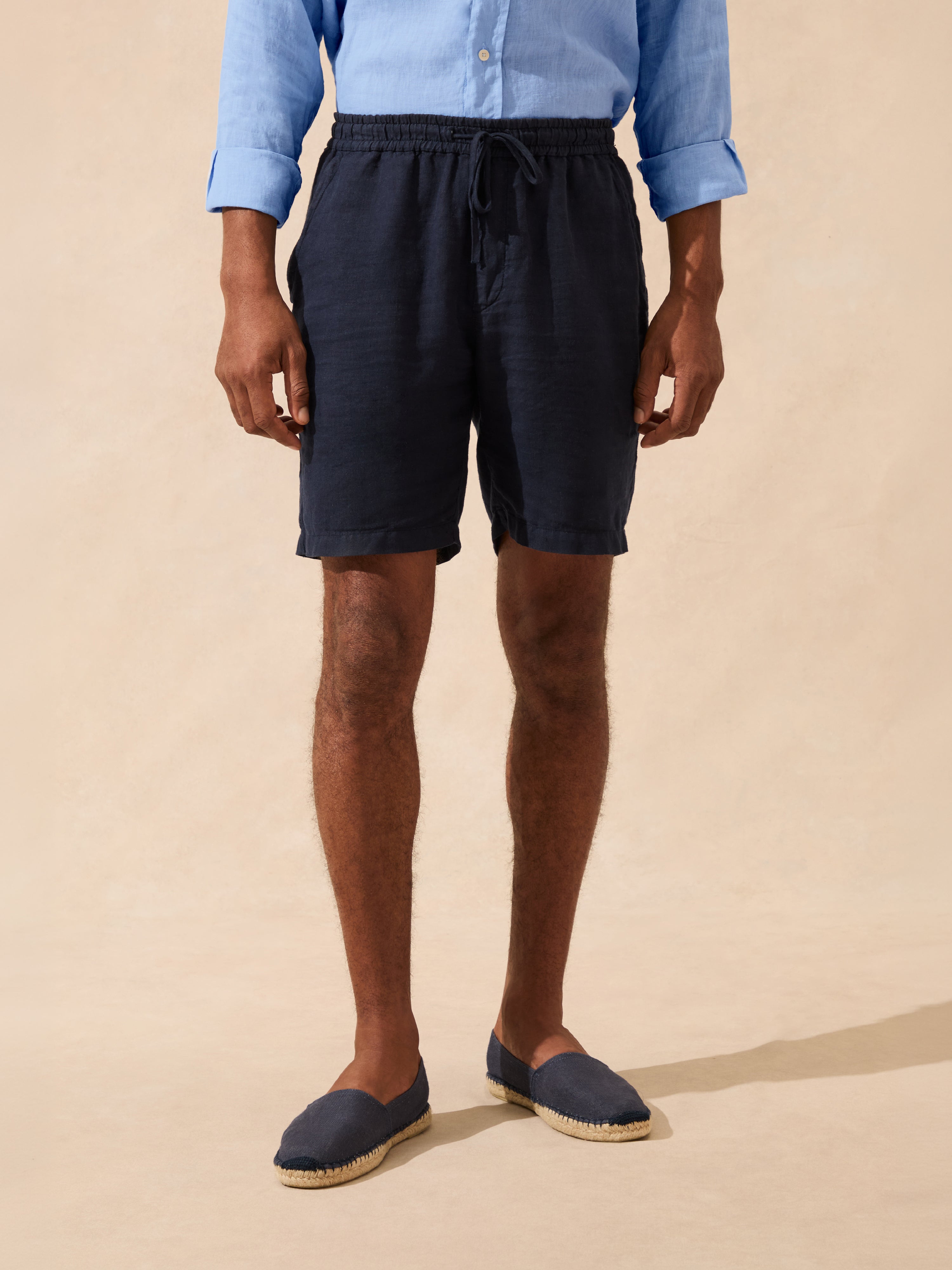 man wearing navy shorts and blue shoes on a beige background