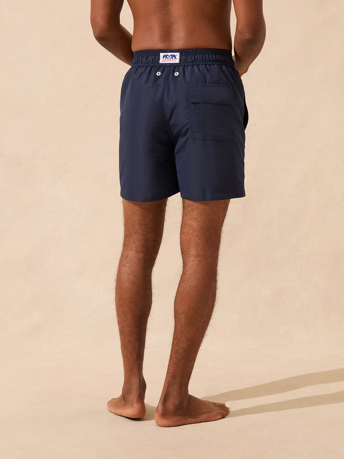 Back view of a man wearing navy swim shorts on a beige background