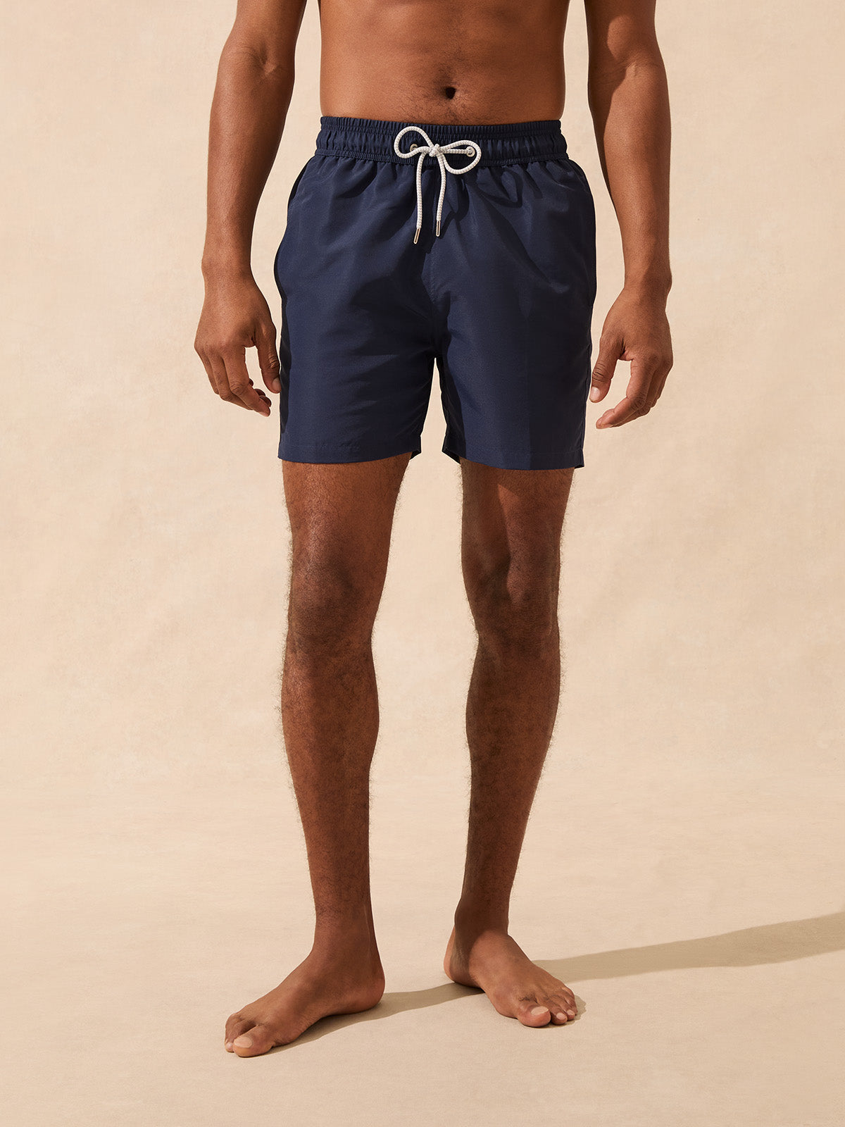 Man wearing navy blue swim shorts on a beige background