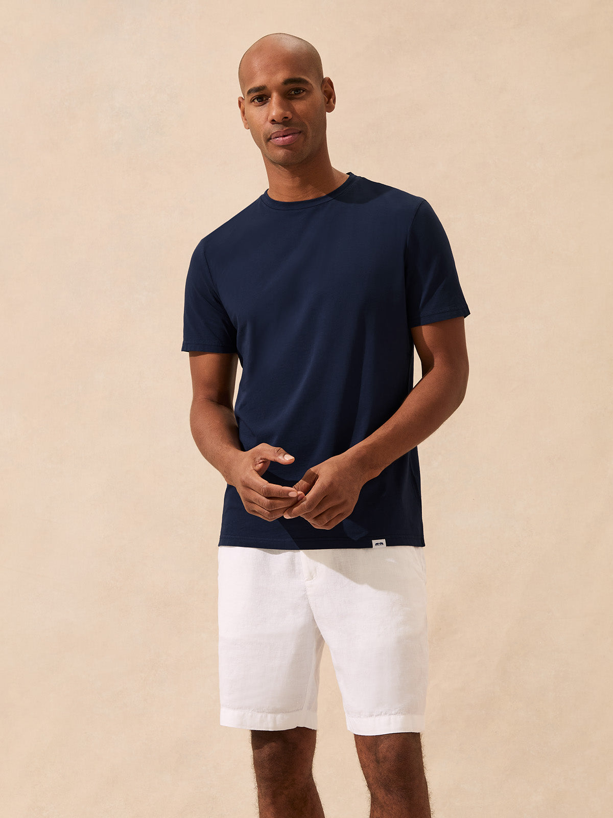 Man wearing a navy t-shirt and white shorts against a beige background