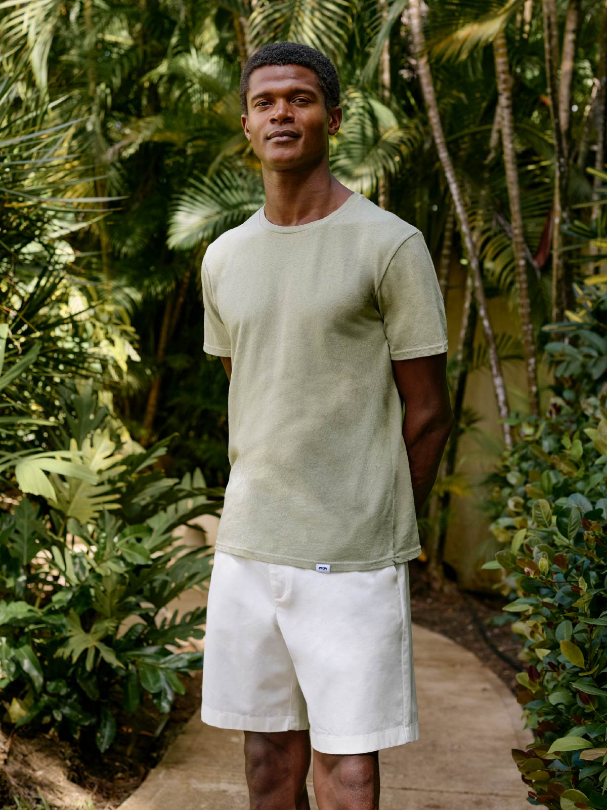 Man standing in a tropical setting wearing a light green t-shirt and white shorts.