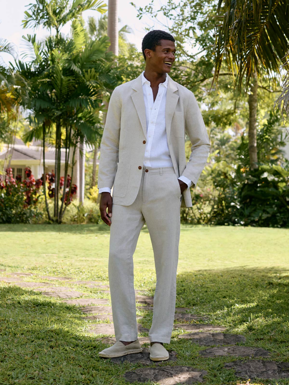 Man in a beige linen suit standing in a garden with greenery around