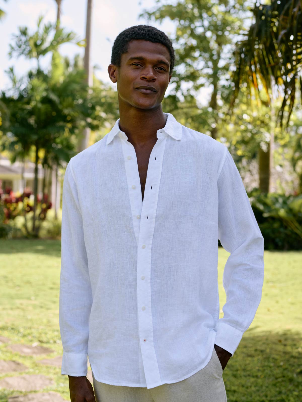 Man wearing a white shirt standing outdoors with greenery in the background