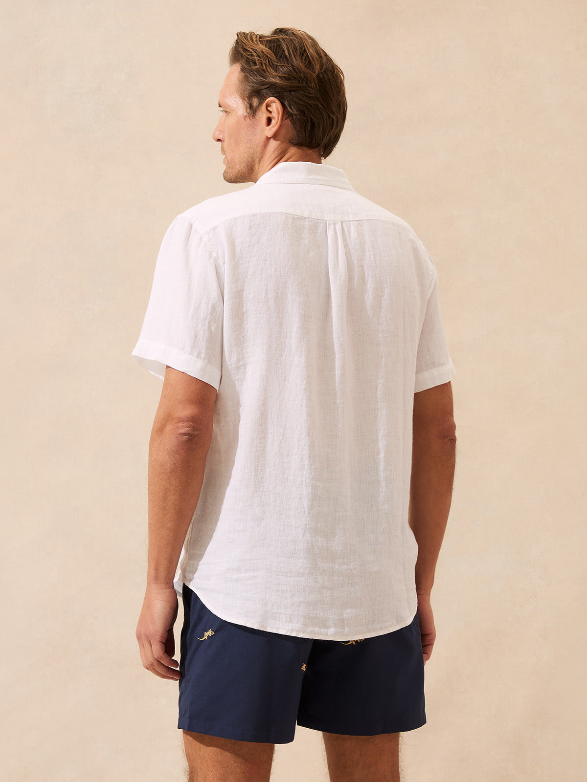 Man wearing a white short-sleeve linen shirt on a beige background