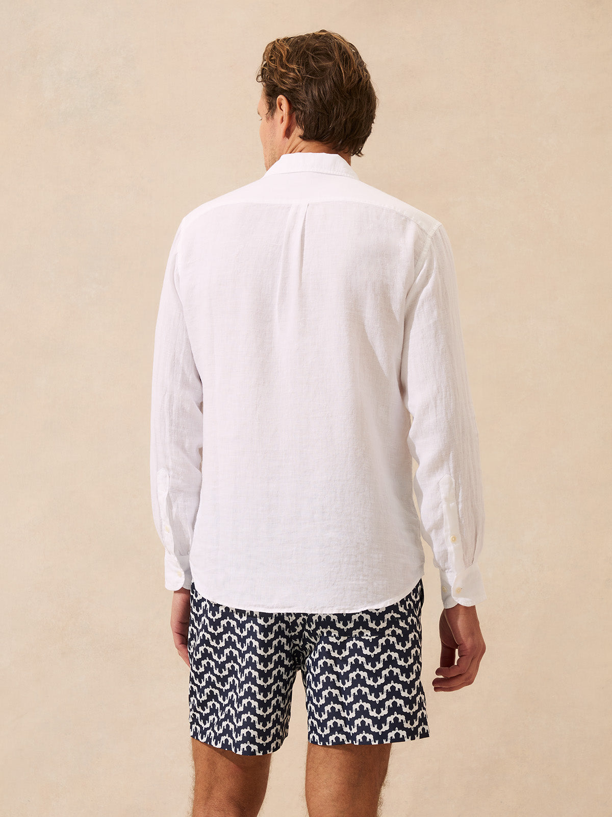 Man wearing a white linen shirt and patterned swim shorts on a beige background