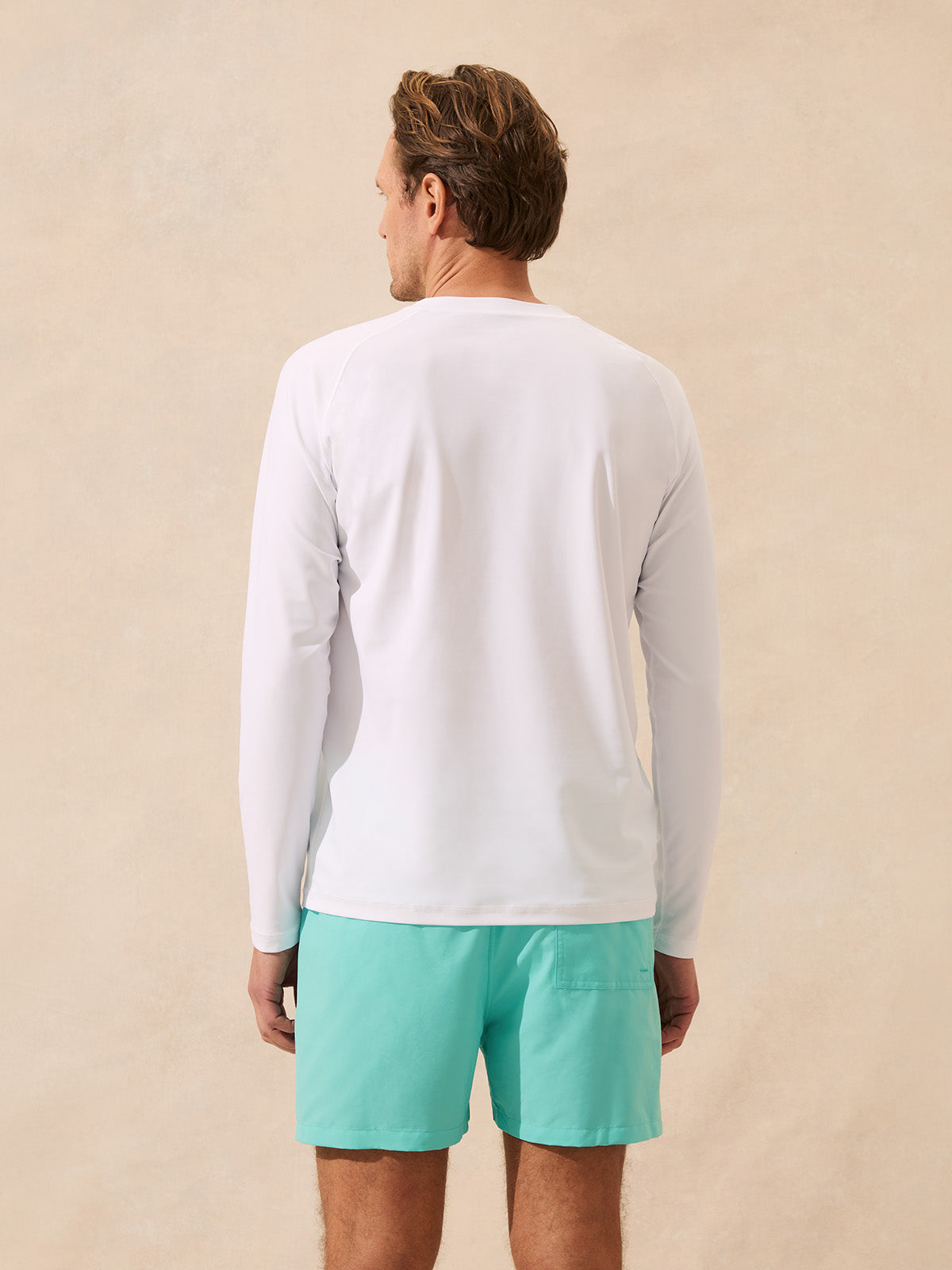 Man wears long sleeve white rash vest against beige background