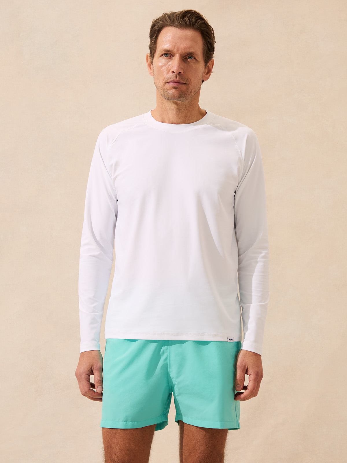 Man wears long sleeve white rash vest against beige background