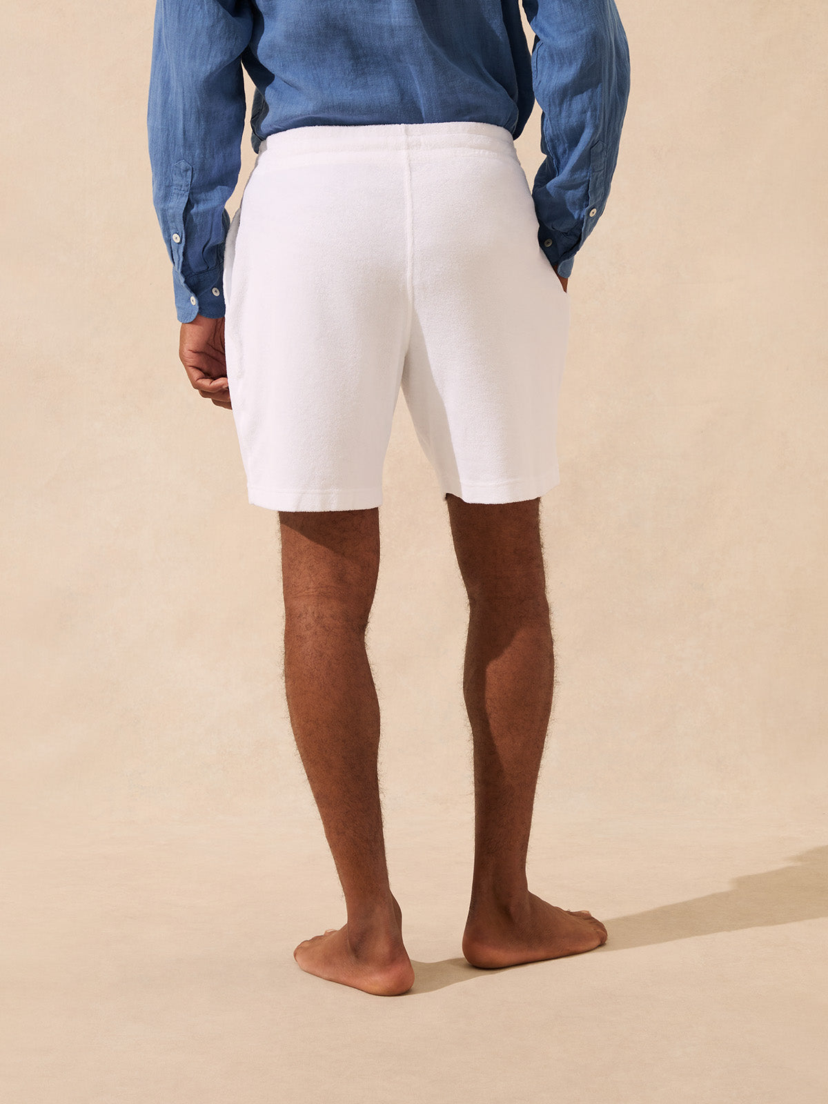 Person wearing white terry shorts and a blue shirt on a beige background