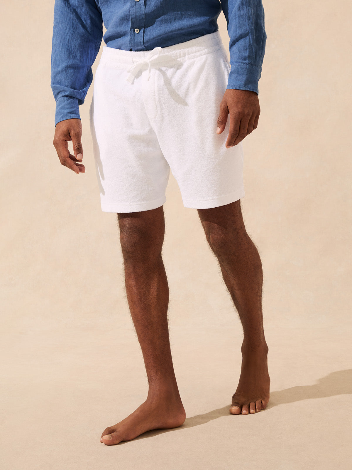 Person wearing white shorts made from terry towelling and a blue shirt on a beige background