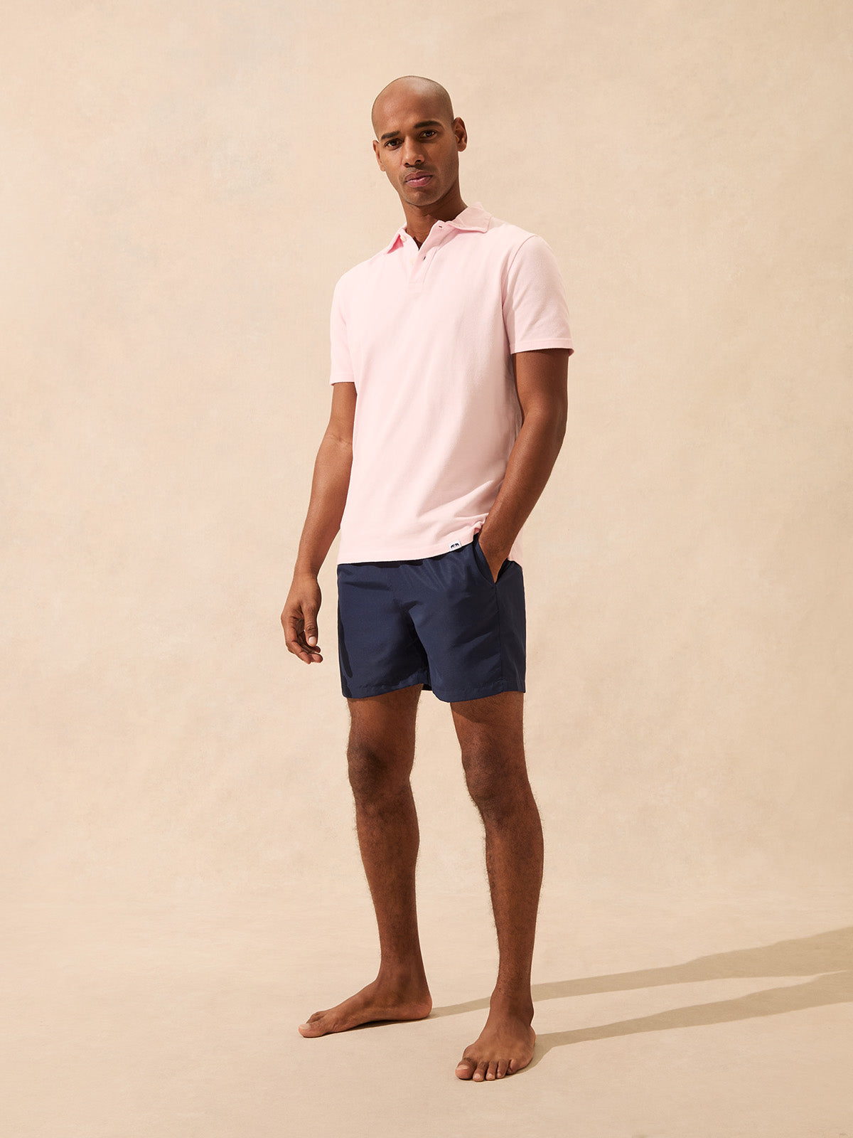 Man wearing a pink polo shirt and navy shorts on a beige background