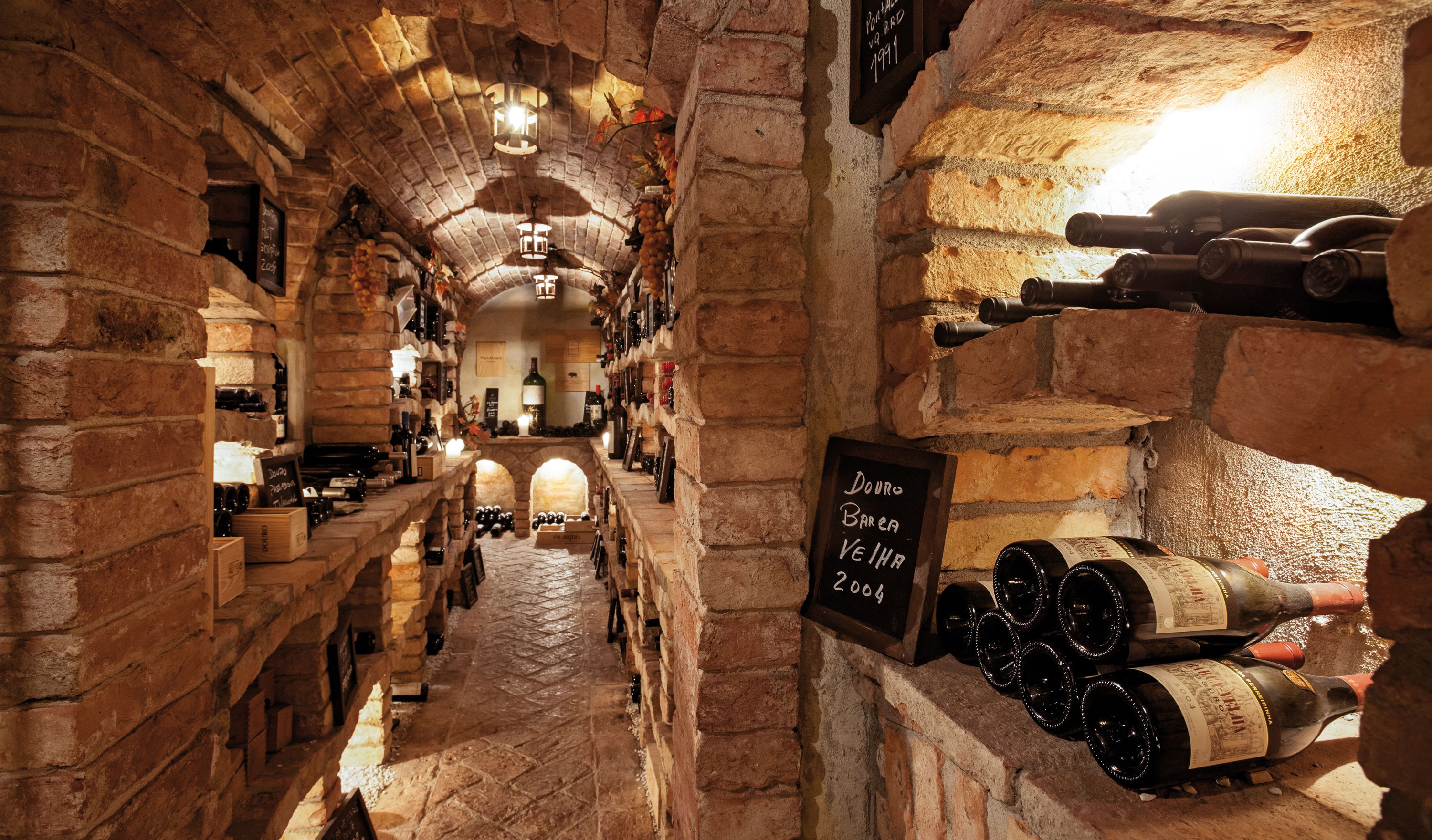 Wine cellar with stone walls and rows of wine bottles.