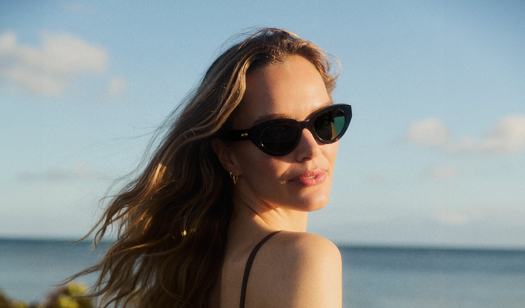 Woman wearing sunglasses with a beach and sky background