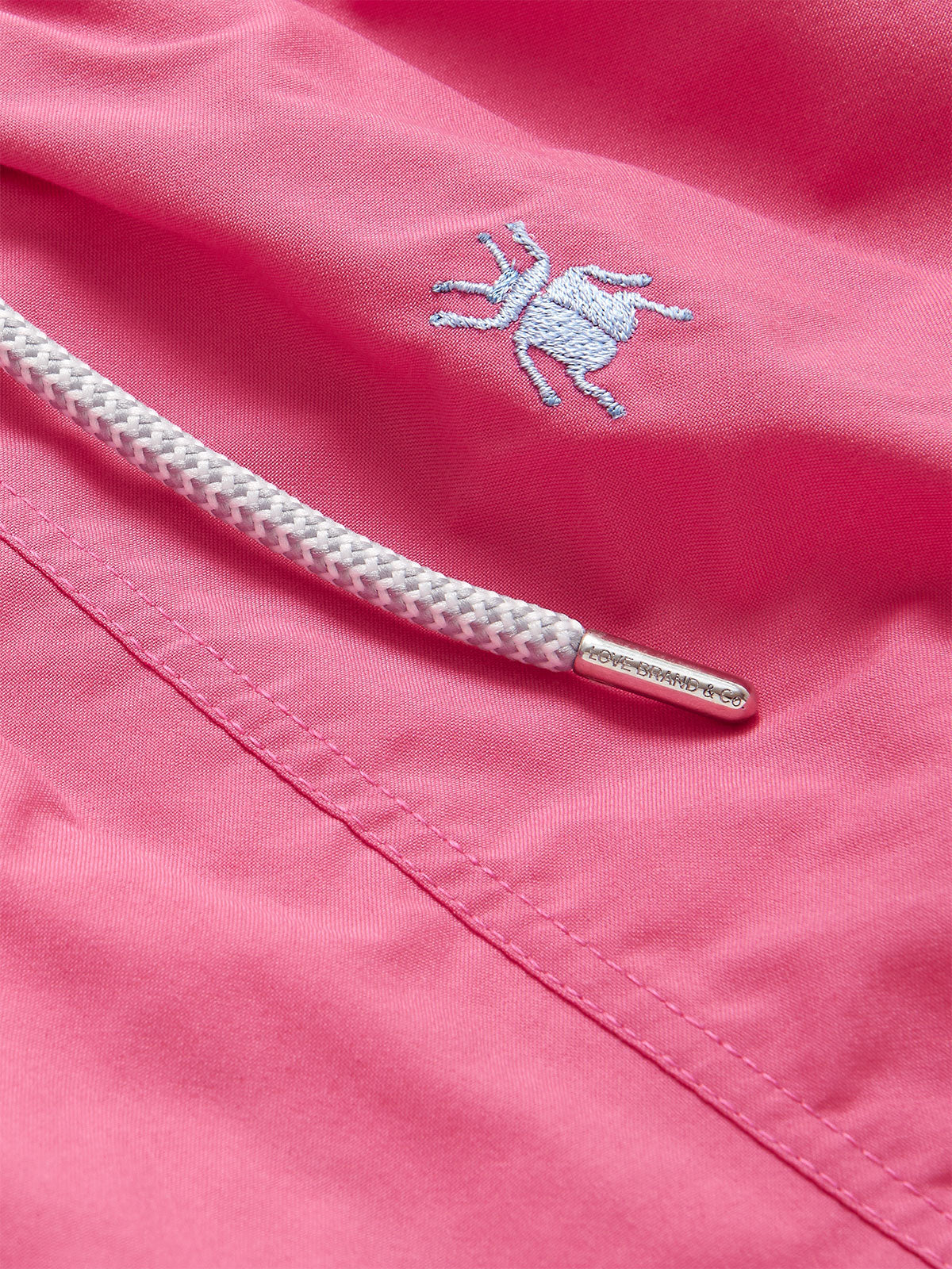 Close-up of Men's Beetle Bum Embroidered Staniel Swim Shorts showcasing the intricate tansy beetle embroidery on a rich Ruby Red base, along with a detailed view of the white drawstring.
