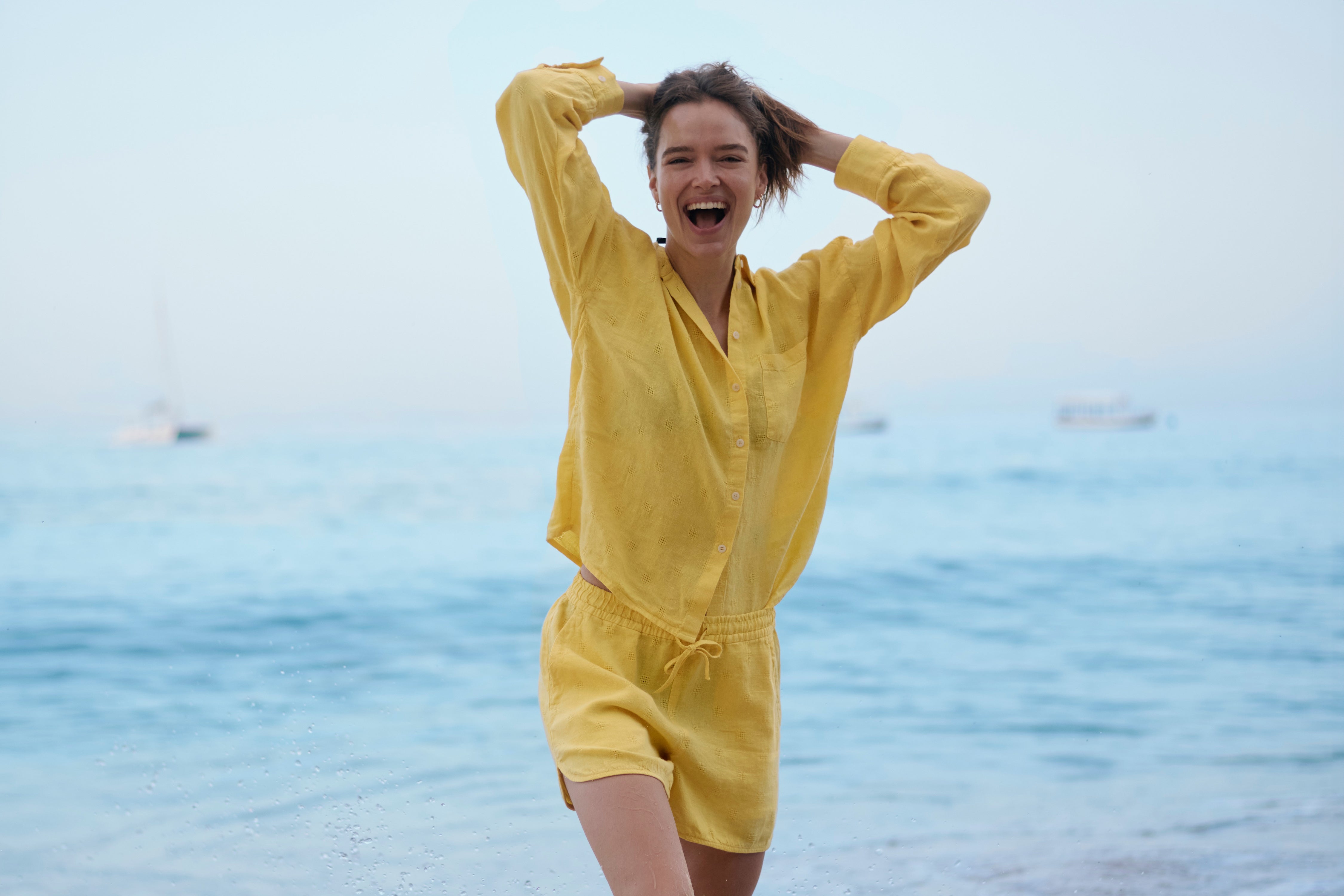 Woman in a yellow linen outfit standing on a beach with ocean in the background